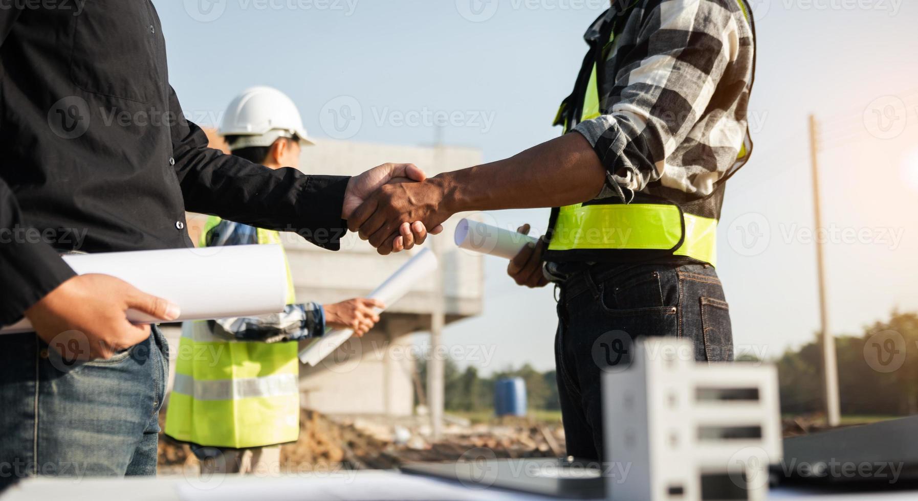 Construction team shake hands greeting start new project plan behind yellow helmet on desk in office center to consults about their building project. photo