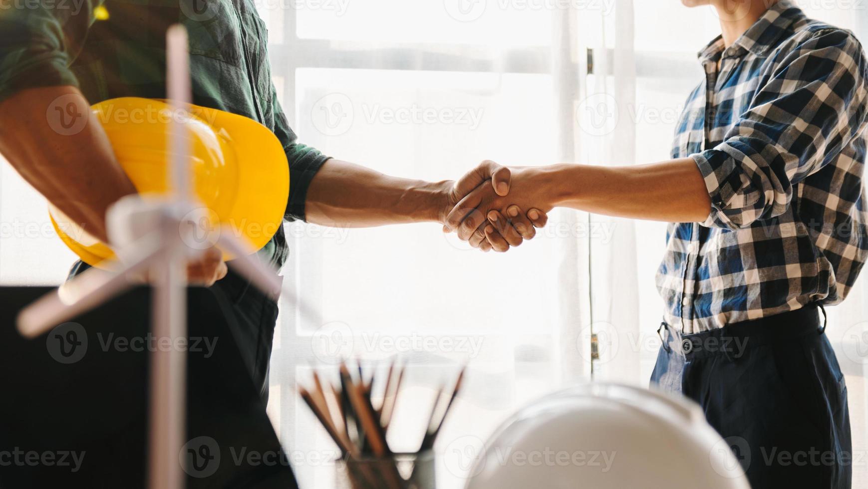 Construction team shake hands greeting start new project plan behind yellow helmet on desk in office to consults about their building project.. photo