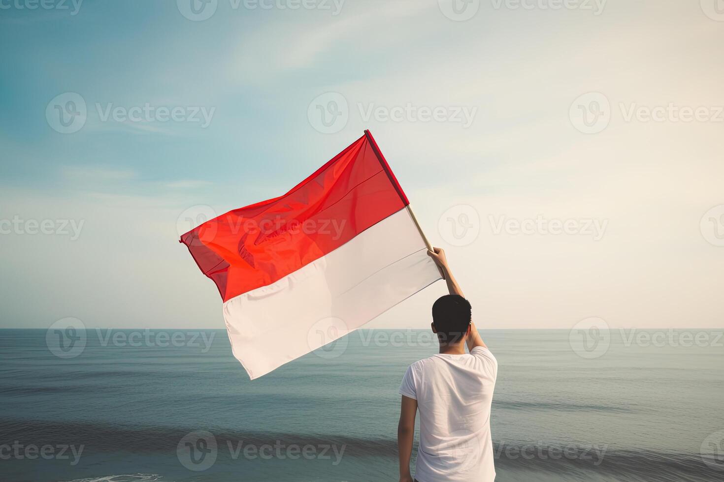 un hombre participación un rojo y blanco Indonesia bandera mirando a el océano. ai generado foto