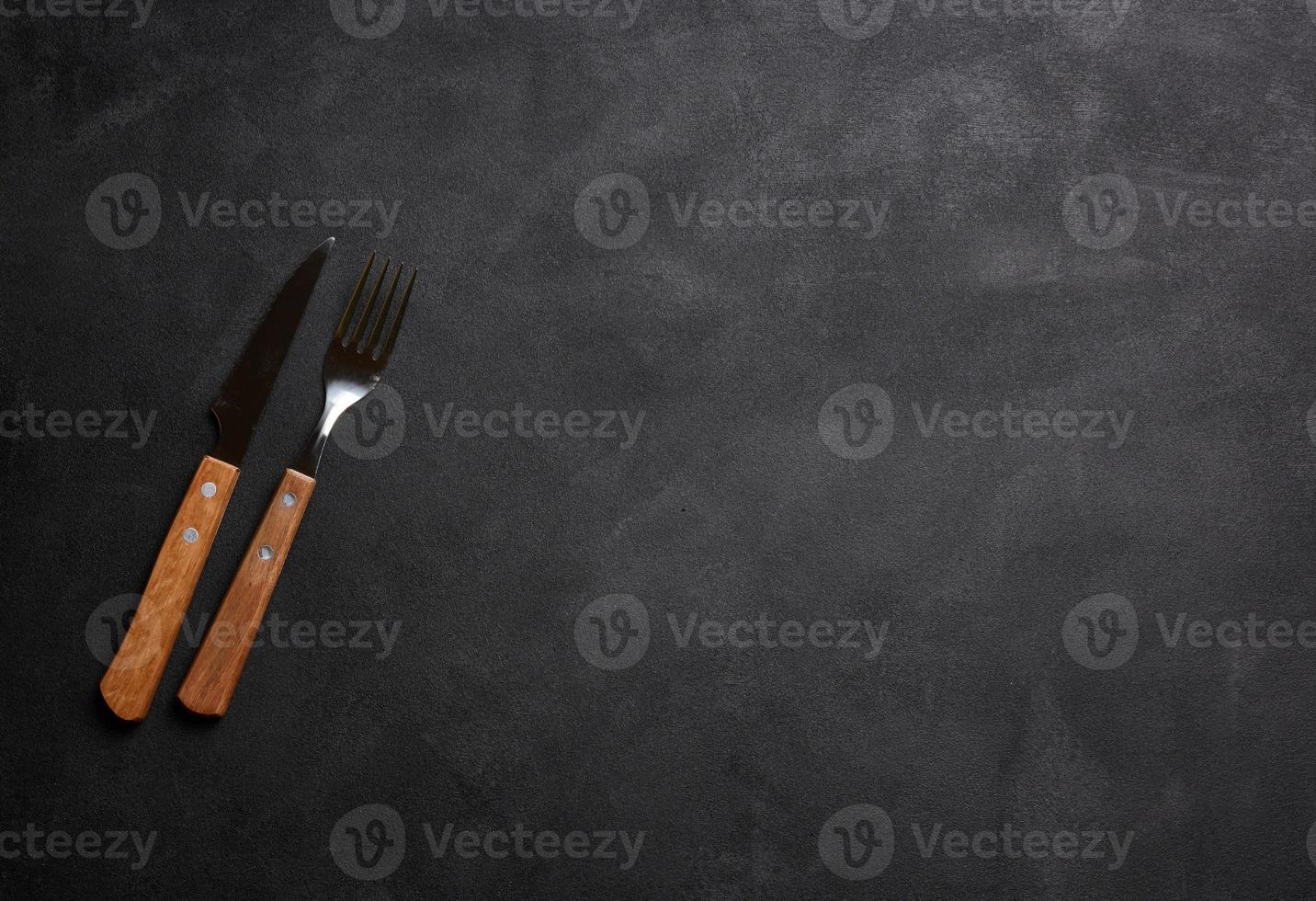 Fork and knife with wooden handle on black background, top view photo