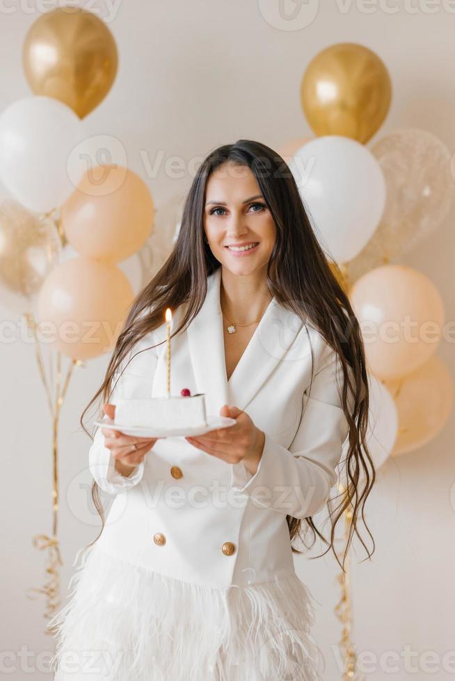 Young caucasian woman holding a birthday cake with a candle in a stylish white dress with feathers photo