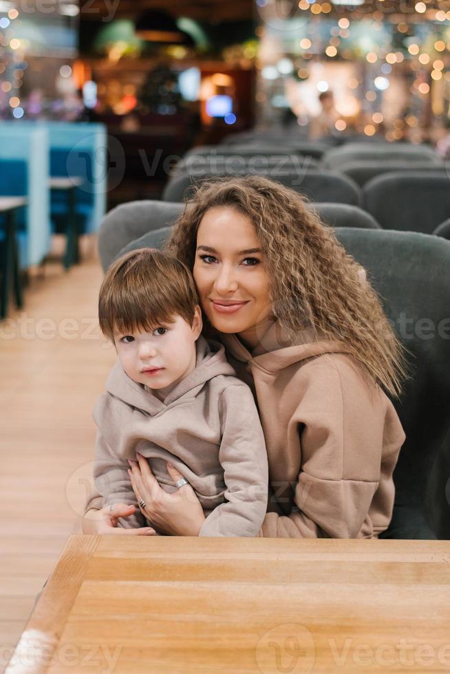 retrato de un hermosa joven madre y un niño de cuatro años hijo en su brazos. el familia es sentado en un café en un silla foto