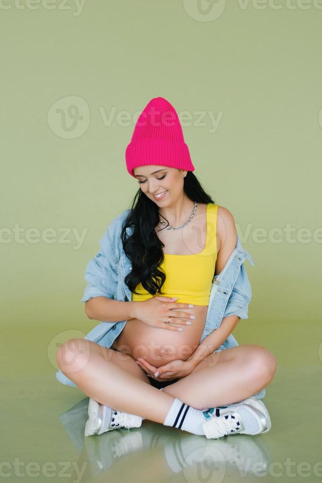 Stylish young expectant mother in stylish clothes on an olive background photo
