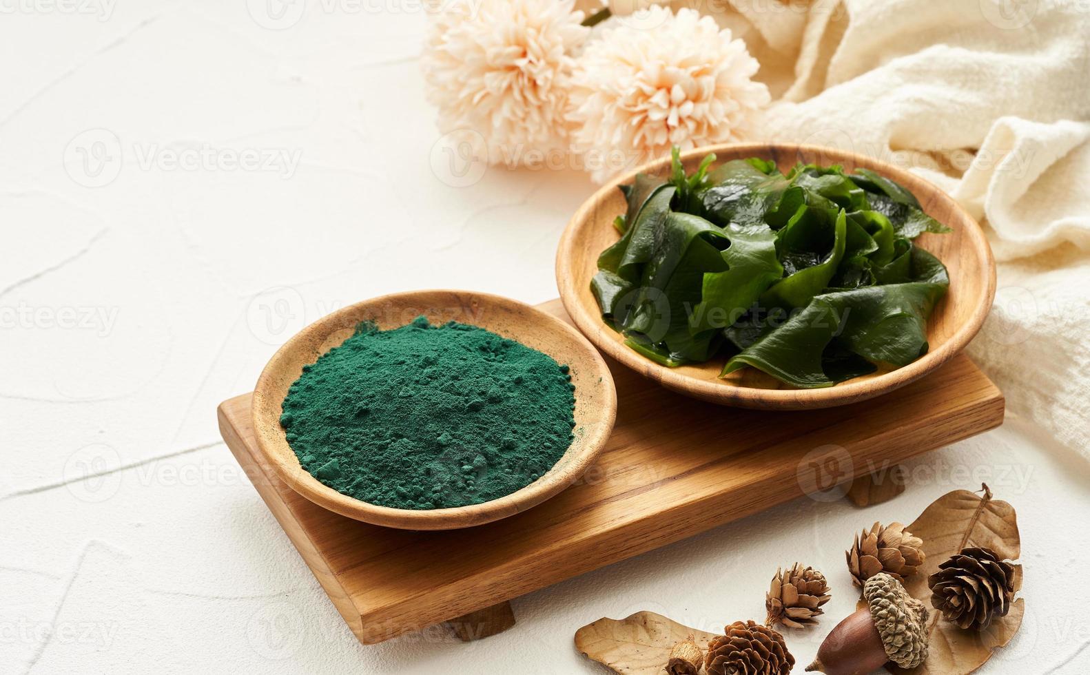 laminaria or kelp seaweed and spirulina powder in wood plate background. spirulina powder with konbu and alga food on white table background. photo