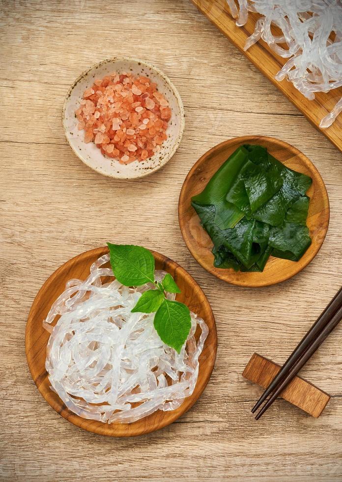 top view or flat lay clear kelp or seaweed noodle in a wooden plate and Himalayan salt on wooden background. glass noodle photo