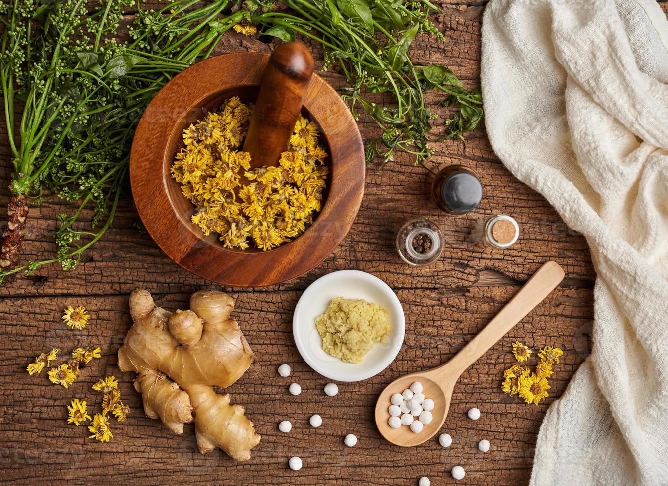 top view homeopathic pills in a wooden spoon and bottles with the herb in a mortar with a pestle on wooden table background photo