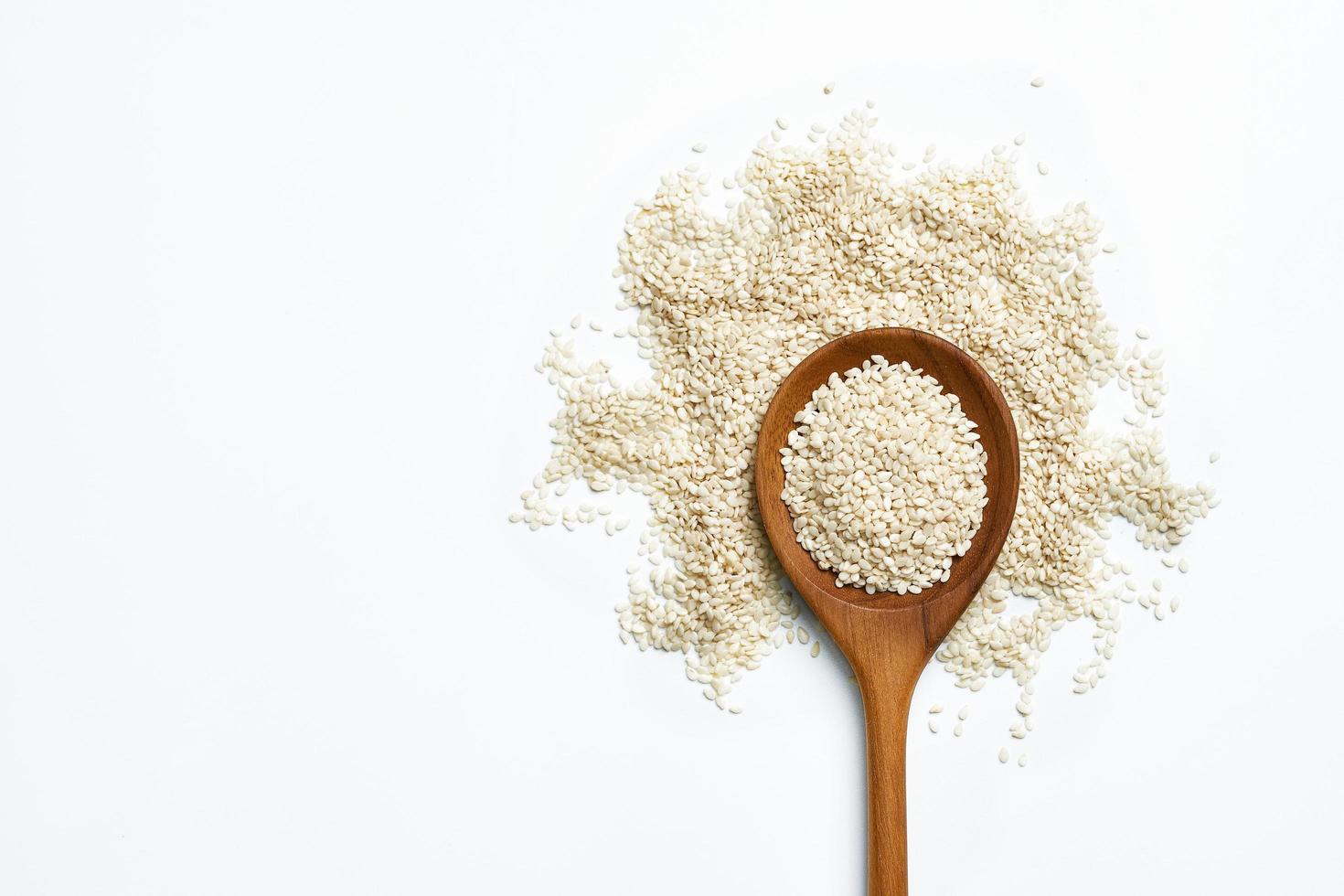 top view white sesame seeds with a wooden spoon on white background with copy space photo