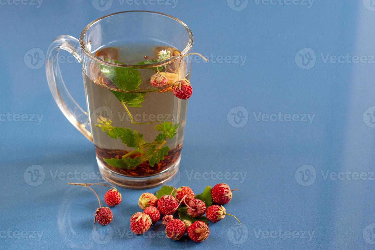 Still life of a mug of herbal tea on blue ceramic tiles with dust texture and reflection. Near scattered strawberries. With space for text. photo