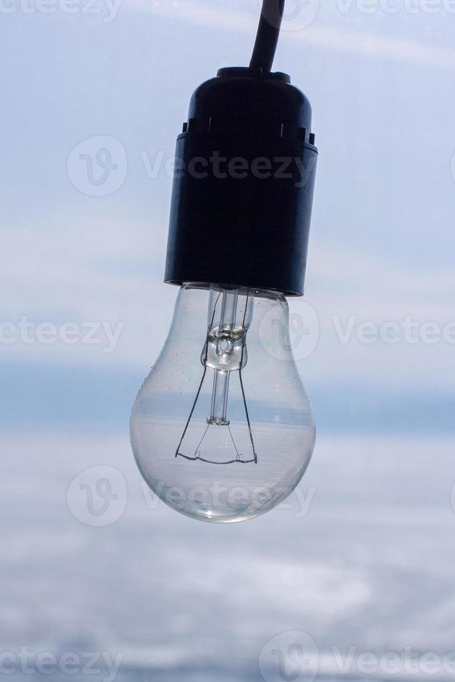 Old dusty incandescent lamp with a cartridge on a blurred background. The spiral is not damaged. Black cartridge and blue background. Vertical. photo