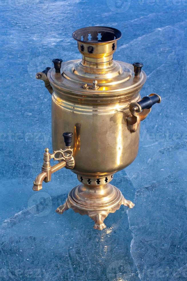 Retro samovar stands on the lake people. A Russian kettle works on firewood. Made of copper and brass. Cracks in the blue ice. Vertical. photo