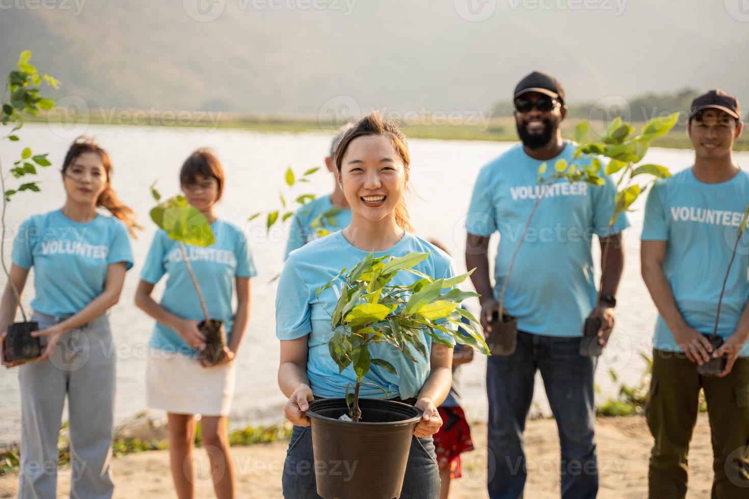 Portrait of young woman with background Group of volunteer holding Pot With Green Plant Smiling To Camera Standing On river. Protection Of Environment And Nature, Ecology Concept. photo