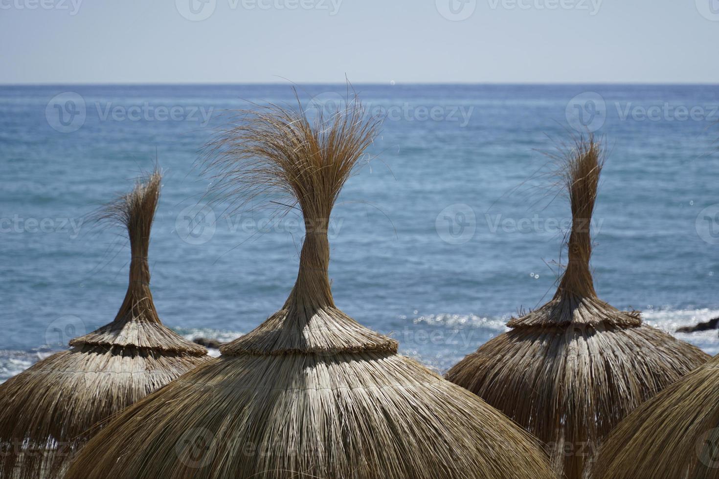 Straw Umbrellas on a Beach, Sea on Second Plan photo