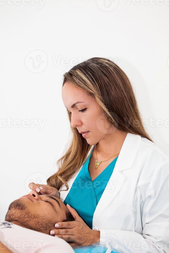 médico ejecutando facial acupuntura en un joven masculino paciente foto