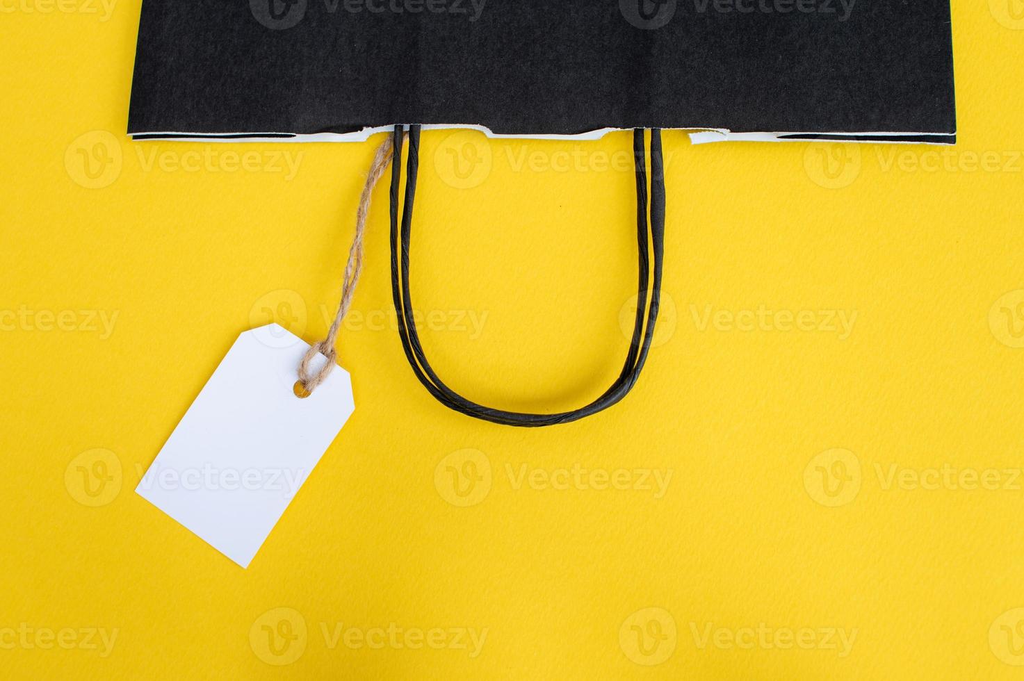 White blank tag with paper black recyclable bag on yellow background. Paper bag handles. photo