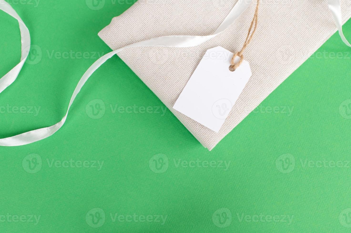 White empty tag on clothes. Mockup of a price tag label on a fabric product. Green background photo