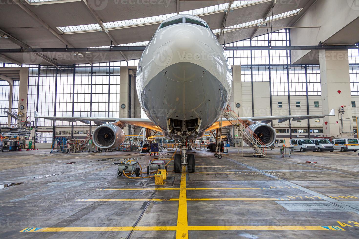 Frontal view to an white and grey colored airplane in maintenance hall photo