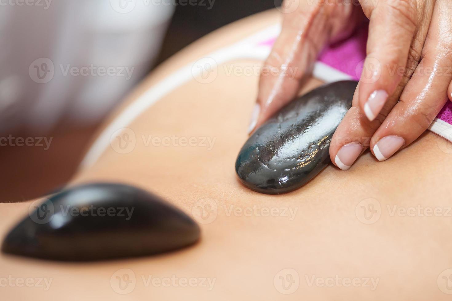 Doctor performing a hot volcanic stones therapy on a young female patient back photo