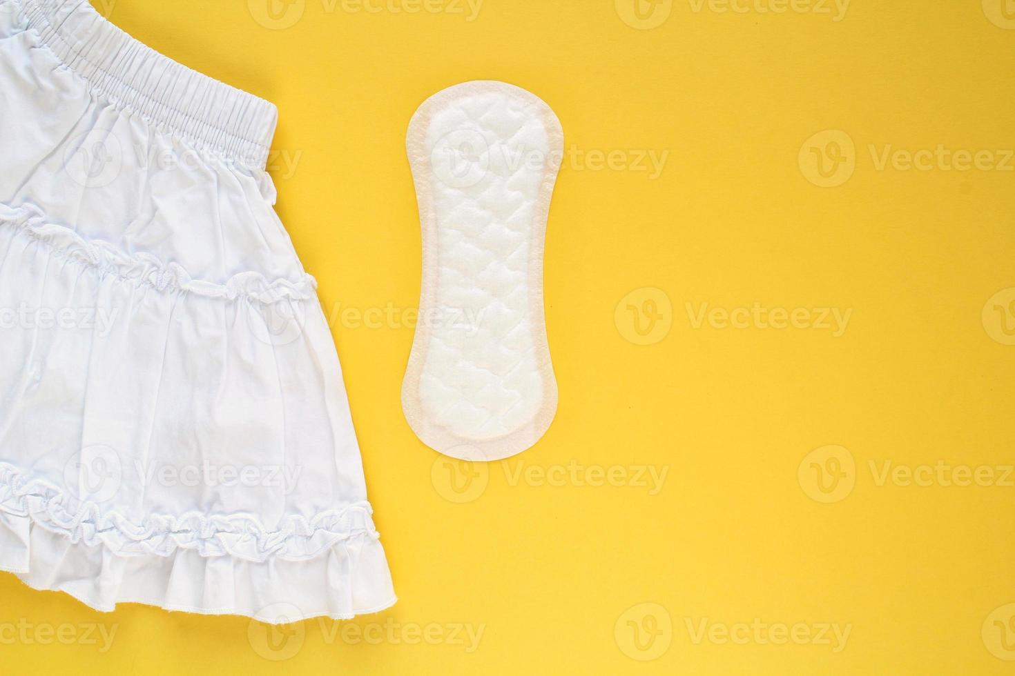 White skirt and woman sanitary pad on yellow background. Female menstruation cycle period. Hygiene concept. Linen and health protection idea. Copy space photo