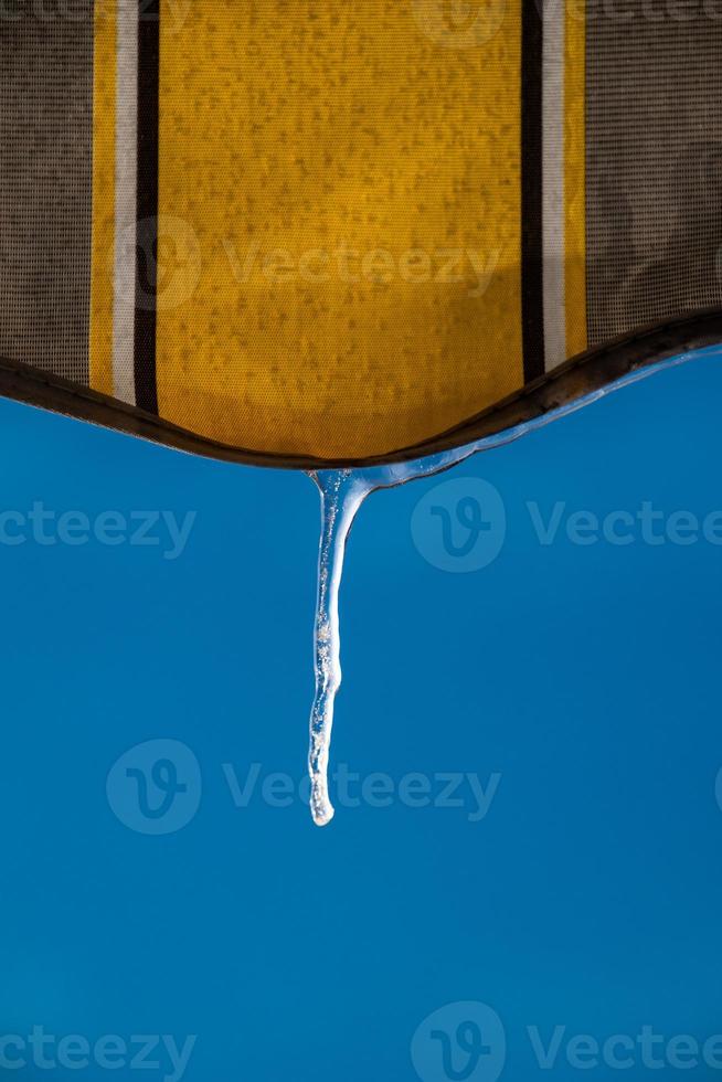an icicle against a blue sky hanging from a yellow awning photo