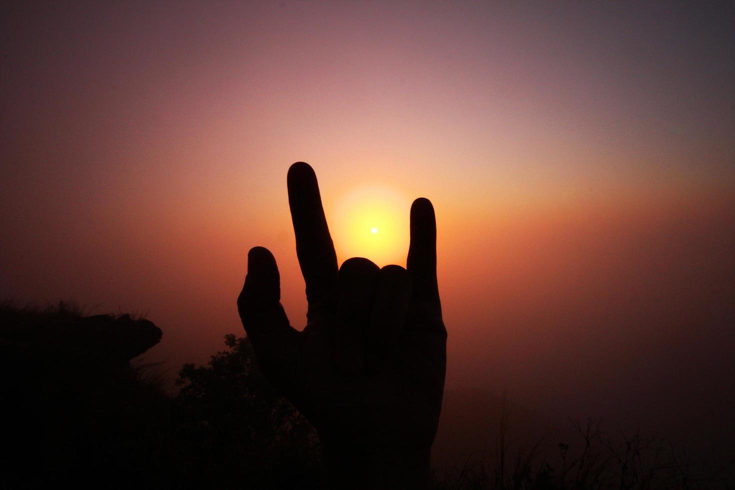 Beautiful silhouette of fingers and hand with valley of mountain in foggy and mist of sunrise shining on the sky photo