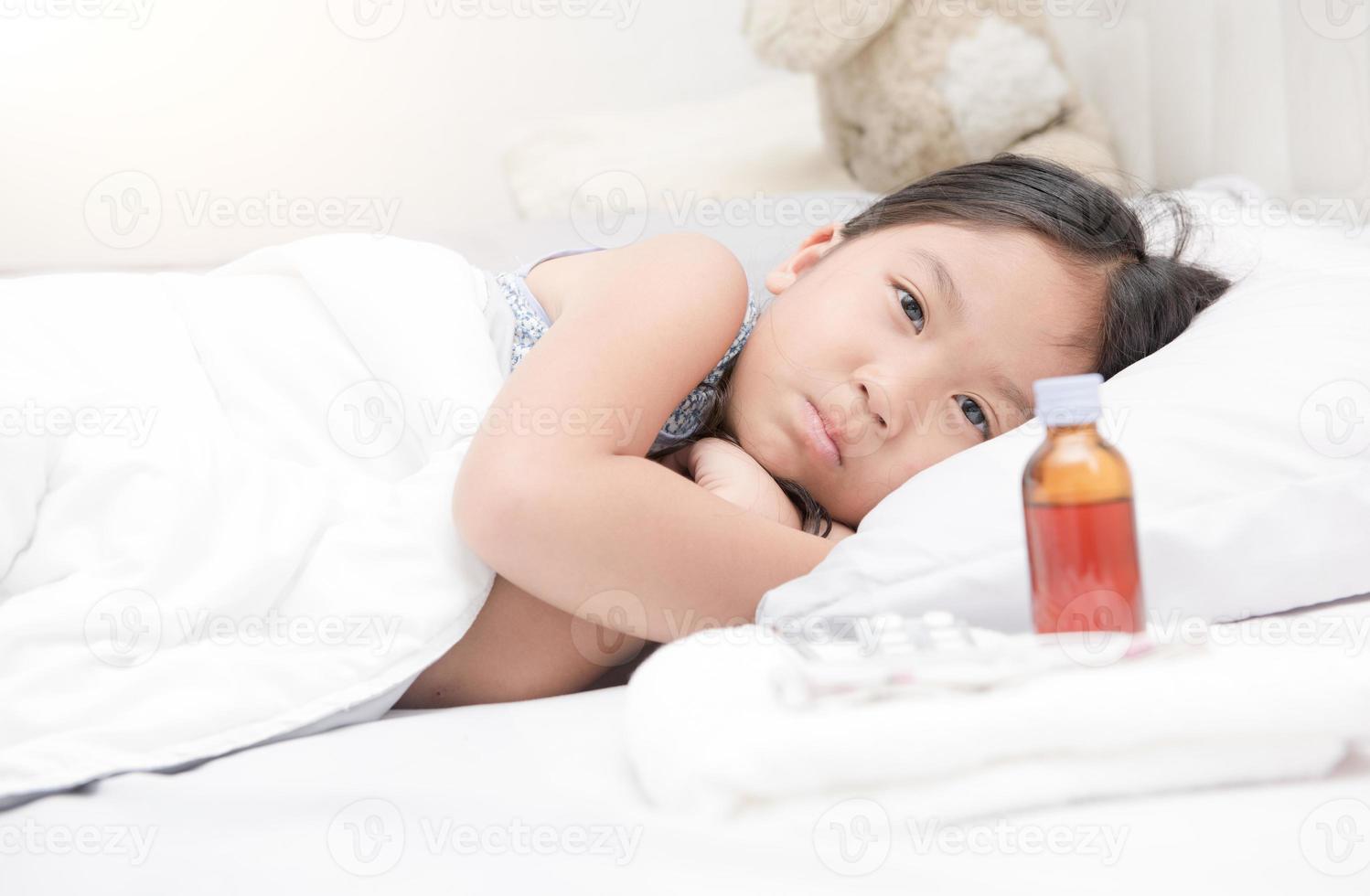 sick girl lying in bed and medicine syrup photo