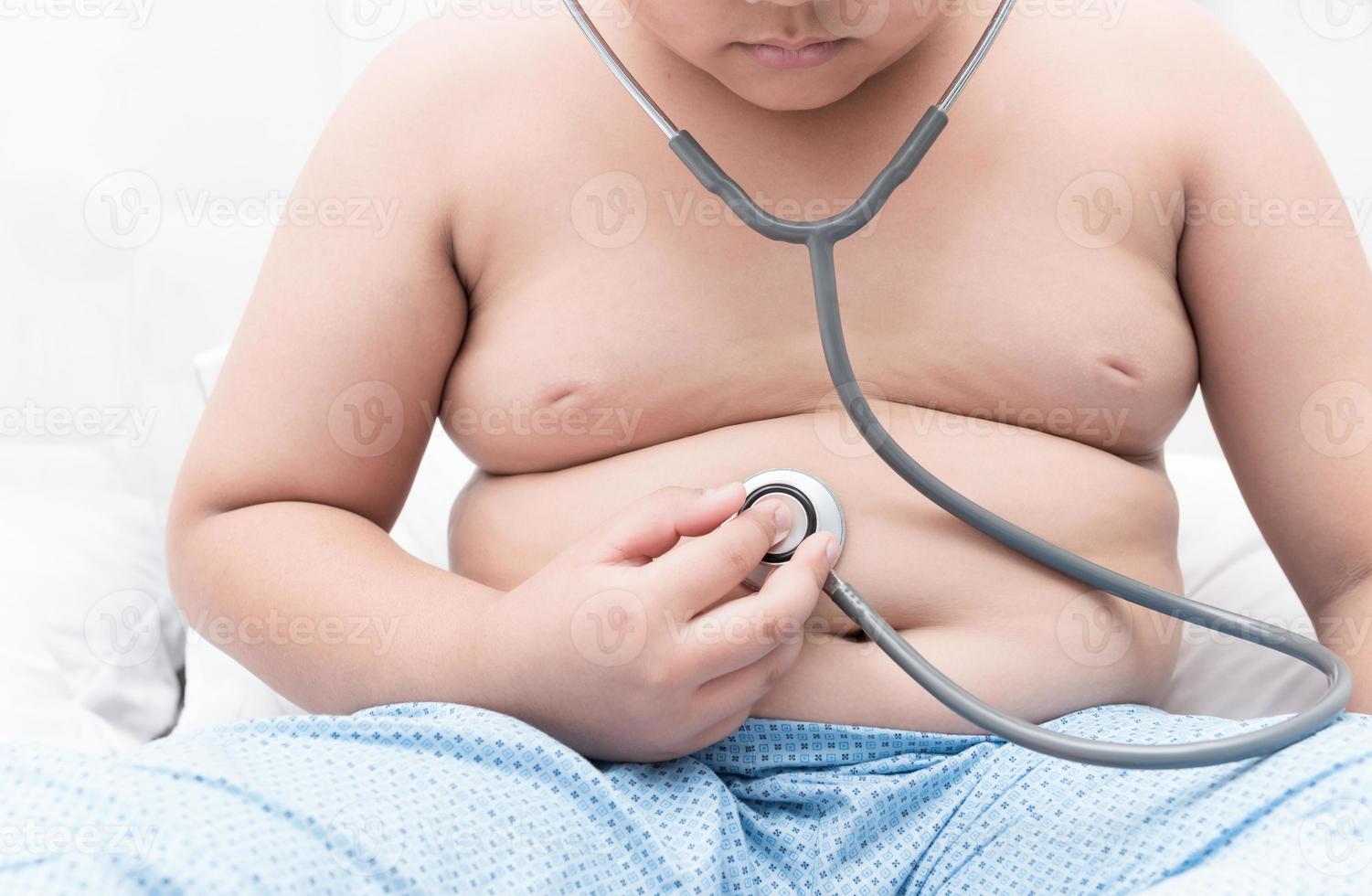 Obese fat boy check stomach by stethoscope. photo