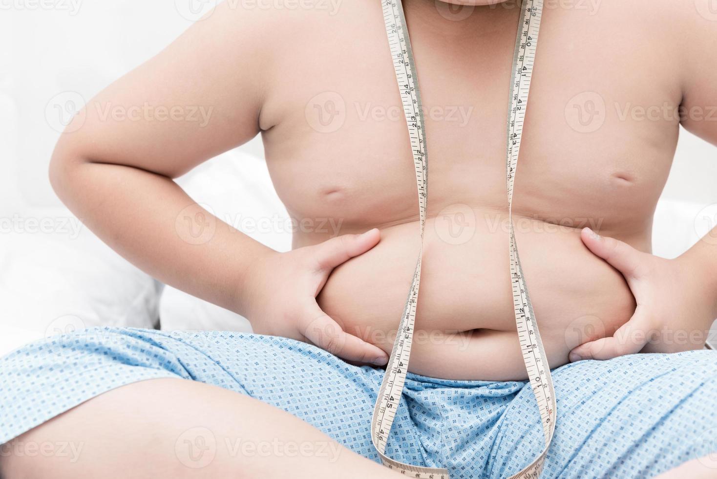 obesity fat boy measuring his belly with measurement tape photo