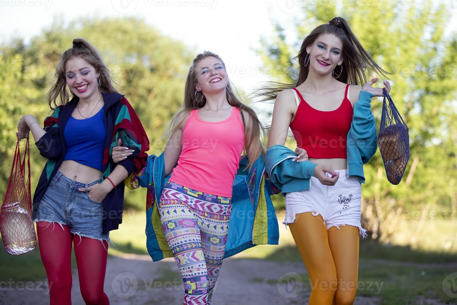 Three beautiful country girls dressed in the style of the nineties are walking along the road. photo