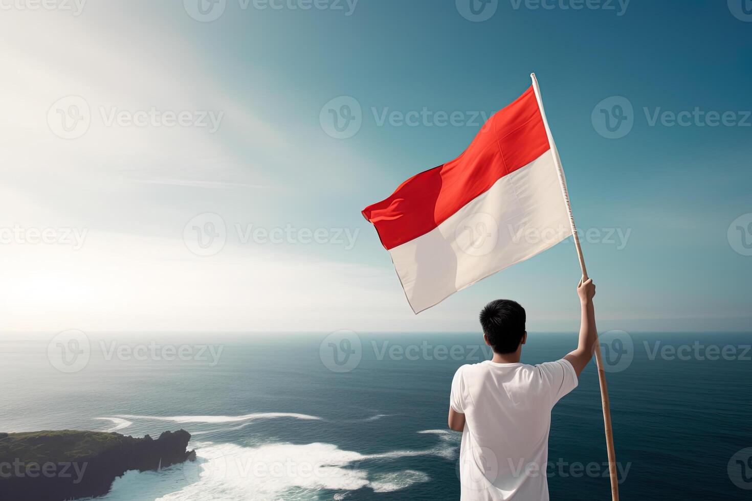 A man holding a red and white Indonesia flag looking at the ocean. photo