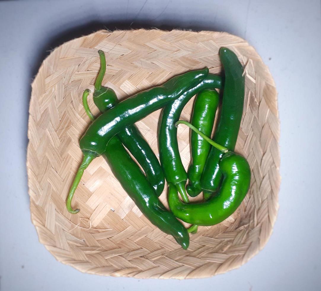 Ripe green chilies in a bamboo basket on a green background. photo