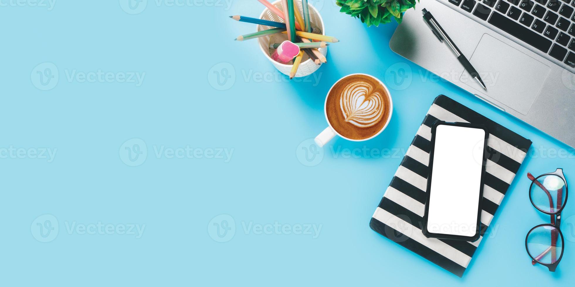 Office desk with laptop computer, Blank screen smart phone, cup of coffee, pen, notebook on blue background, Top view with copy space, Mock up. photo