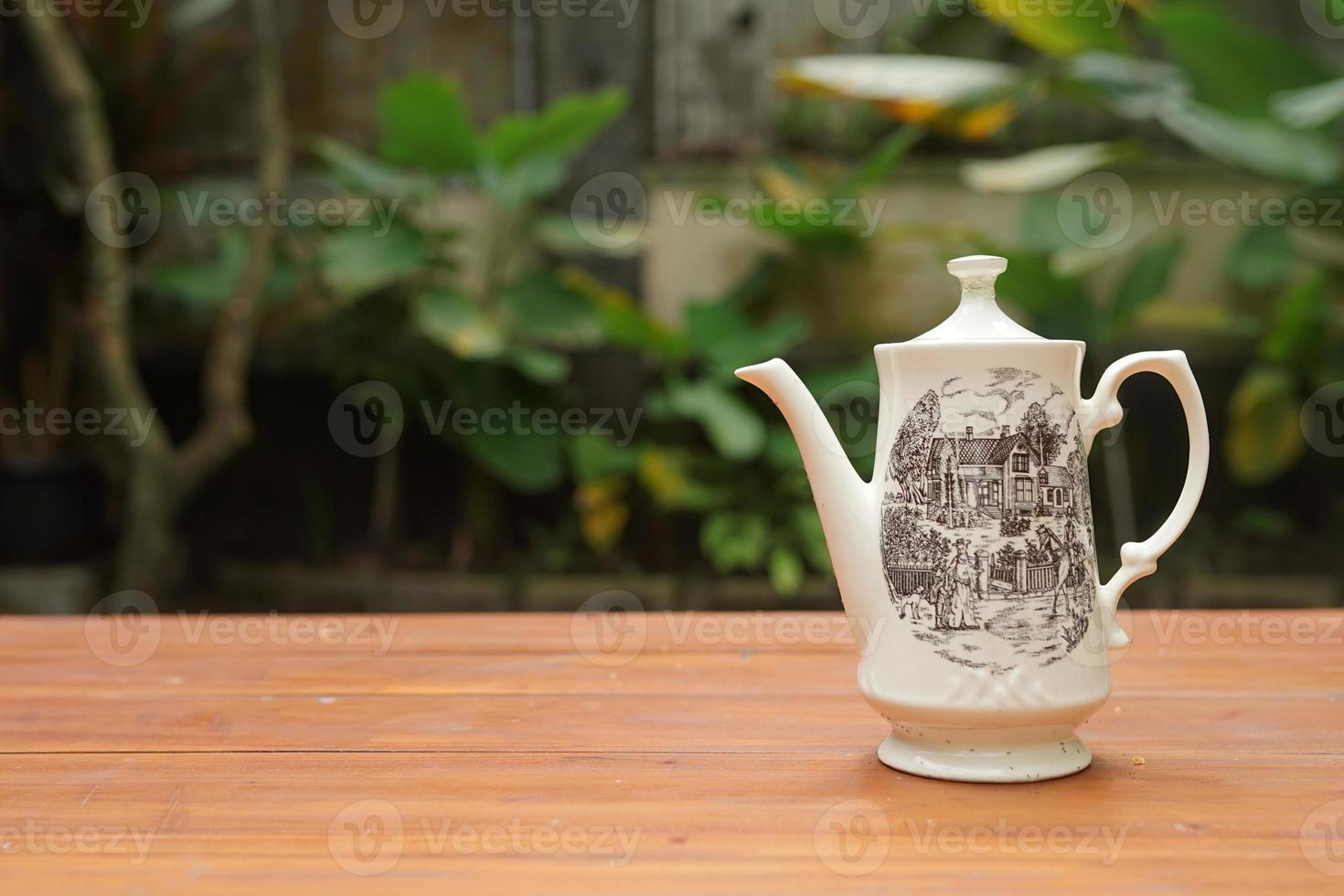 ceramic teapot on wooden table with garden background photo