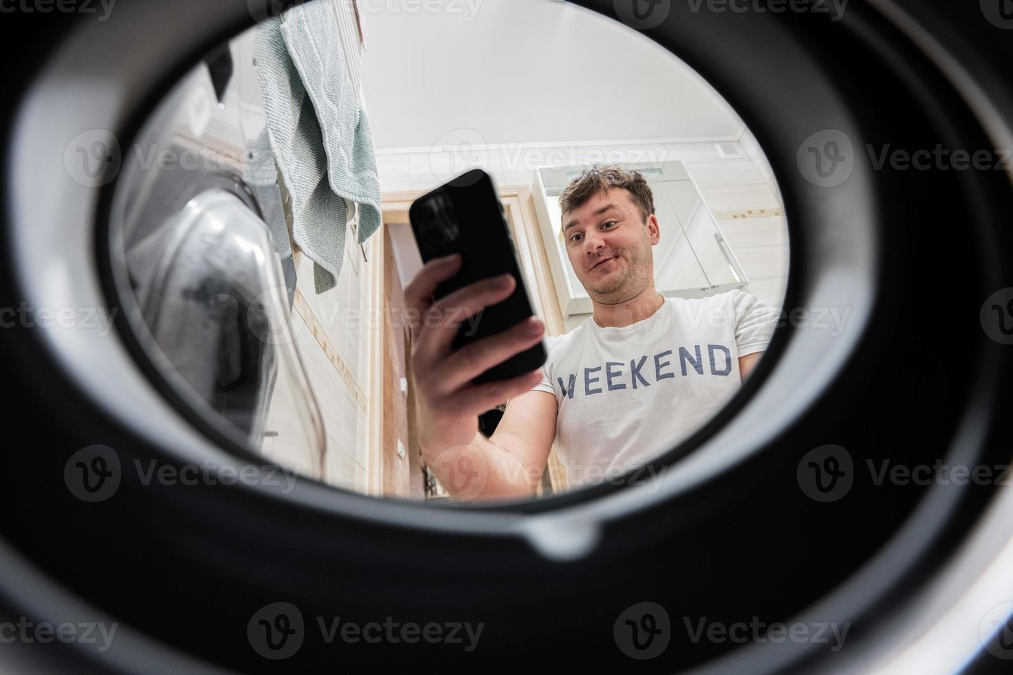 Man with mobile phone, view from washing machine inside. Male does laundry daily routine. photo