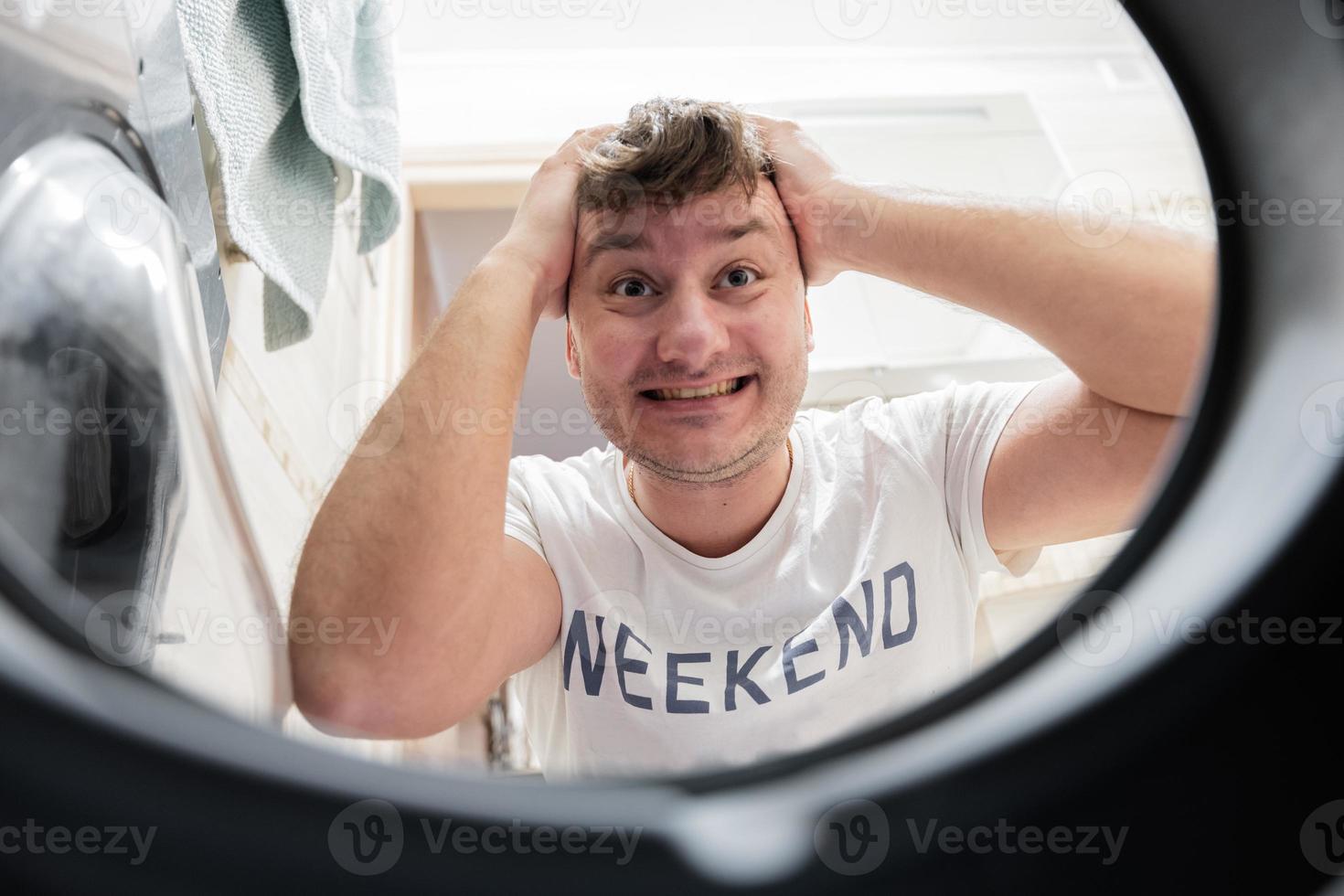 Man view from washing machine inside. Male does laundry daily routine. Put his hands on head in frustration. photo