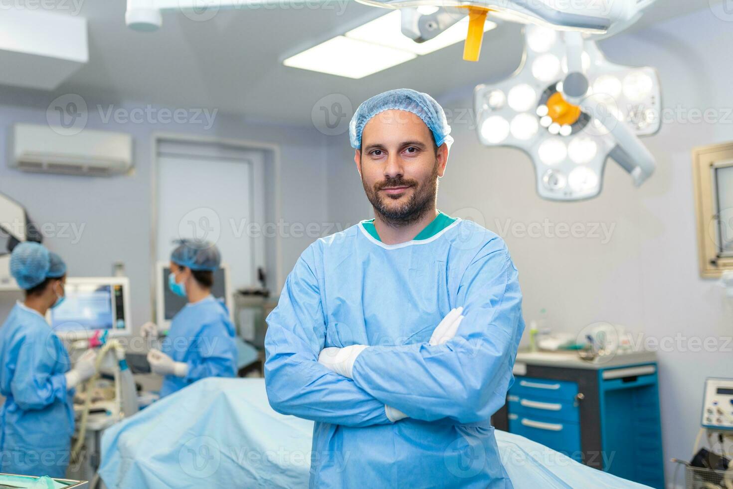 Portrait of male surgeon standing with arms crossed in operation theater at hospital. Team surgeons are performing an operation, middle aged doctor is looking at camera, in a modern operating room photo