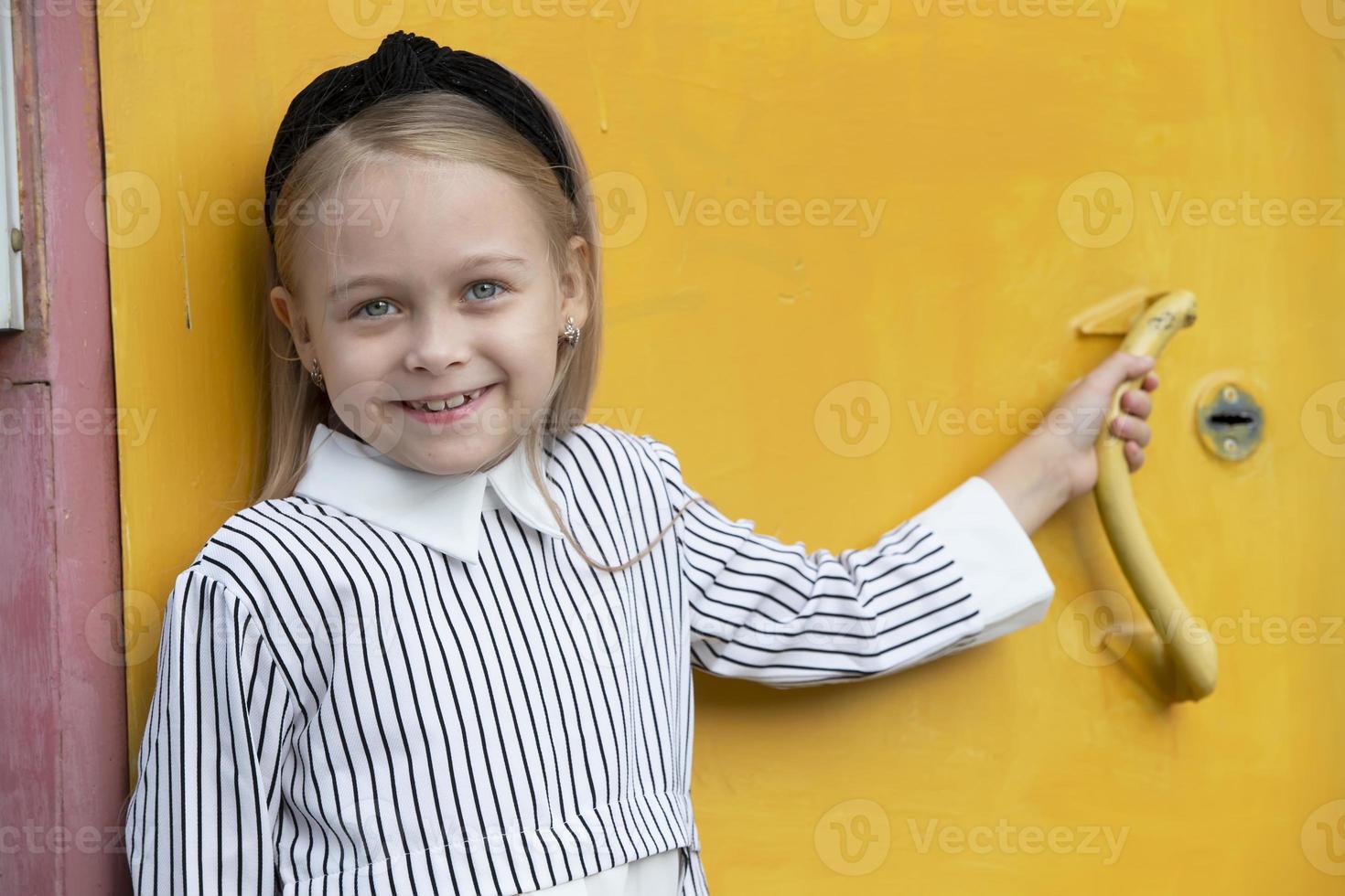 un contento pequeño niña sonrisas a el cámara en contra el amarillo pared. foto