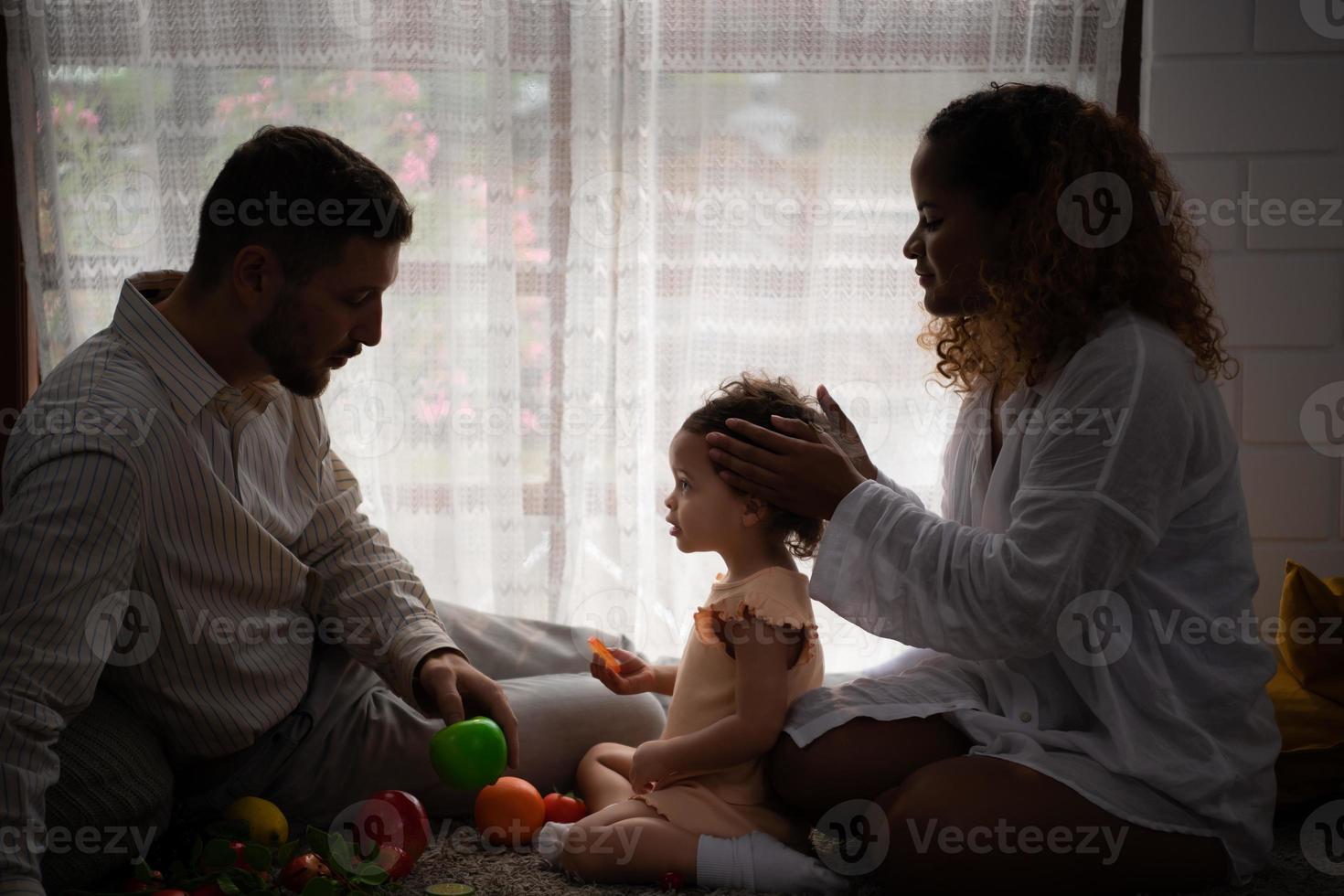 padres y niños relajarse en el vivo habitación de el casa. reloj bebé felizmente jugar con su favorito juguete. foto