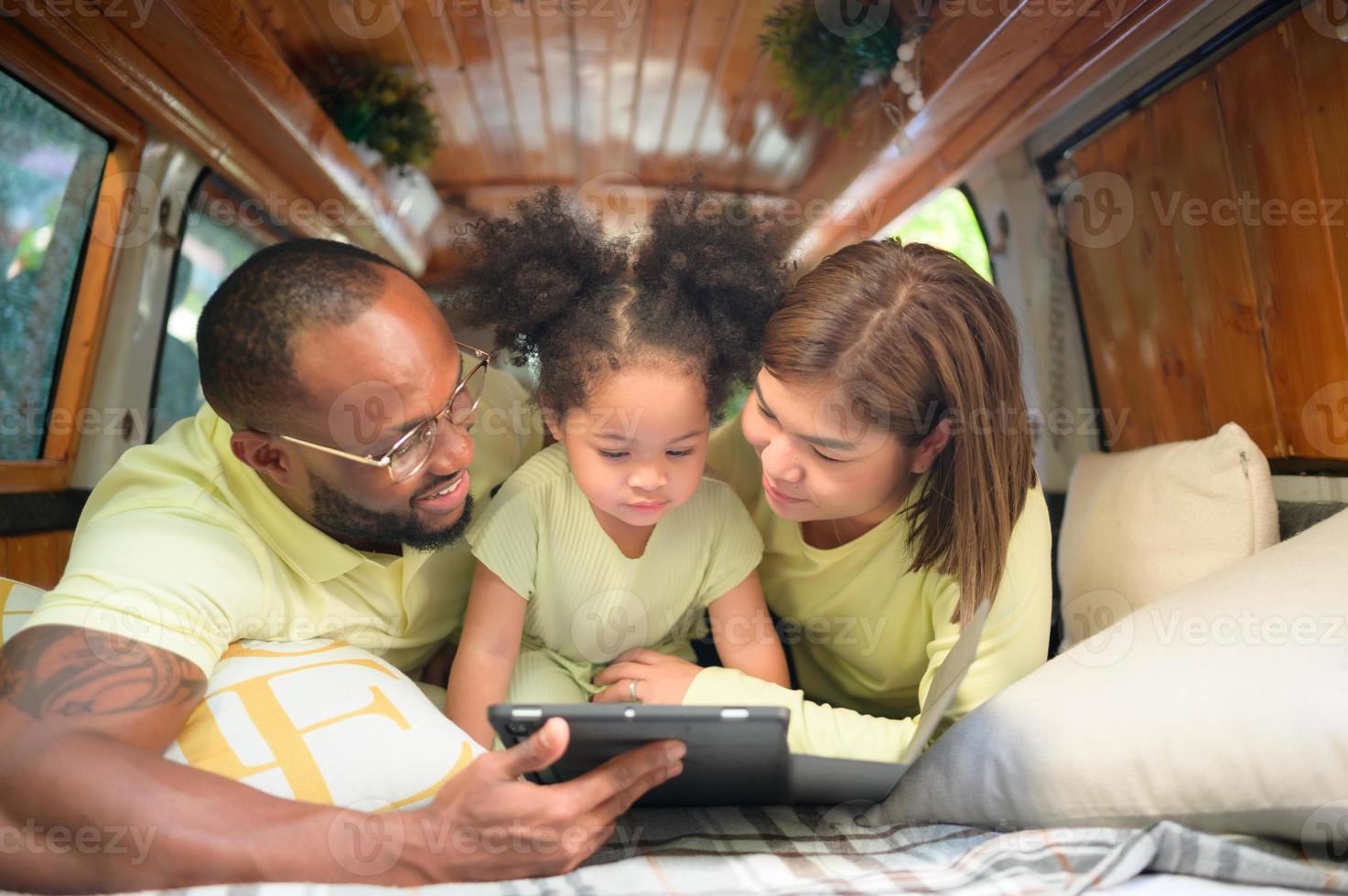 The back of a white classic van, little kids play and learn about the world on their tablet with parents taking care of helping. photo