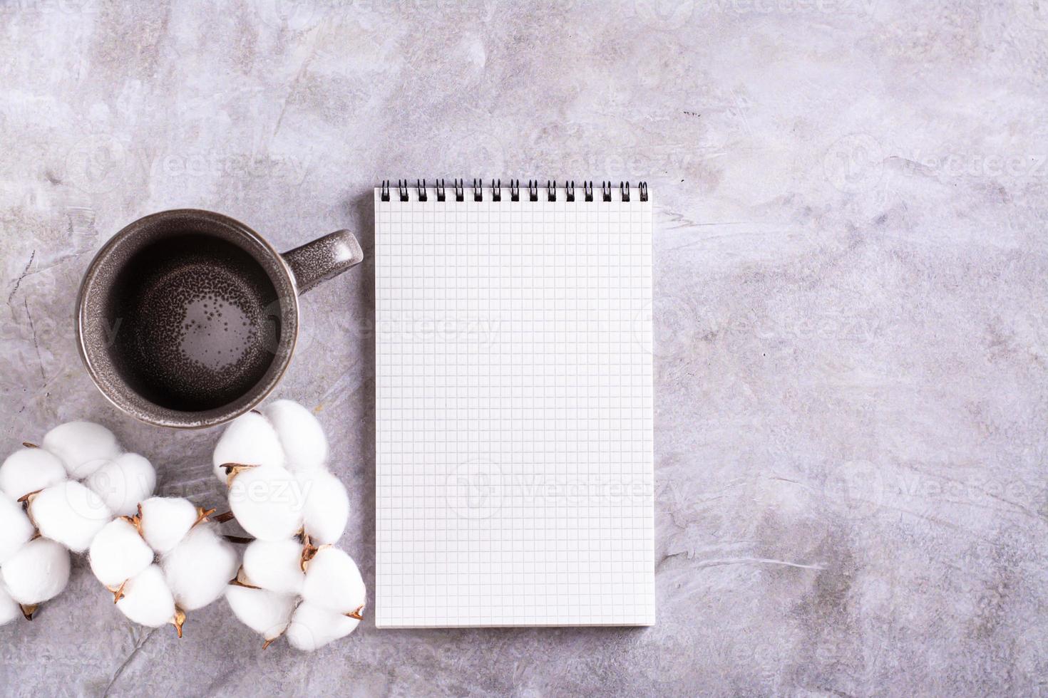 Mockup of a blank open notebook, an empty mug and a branch of cotton on a gray background top view photo