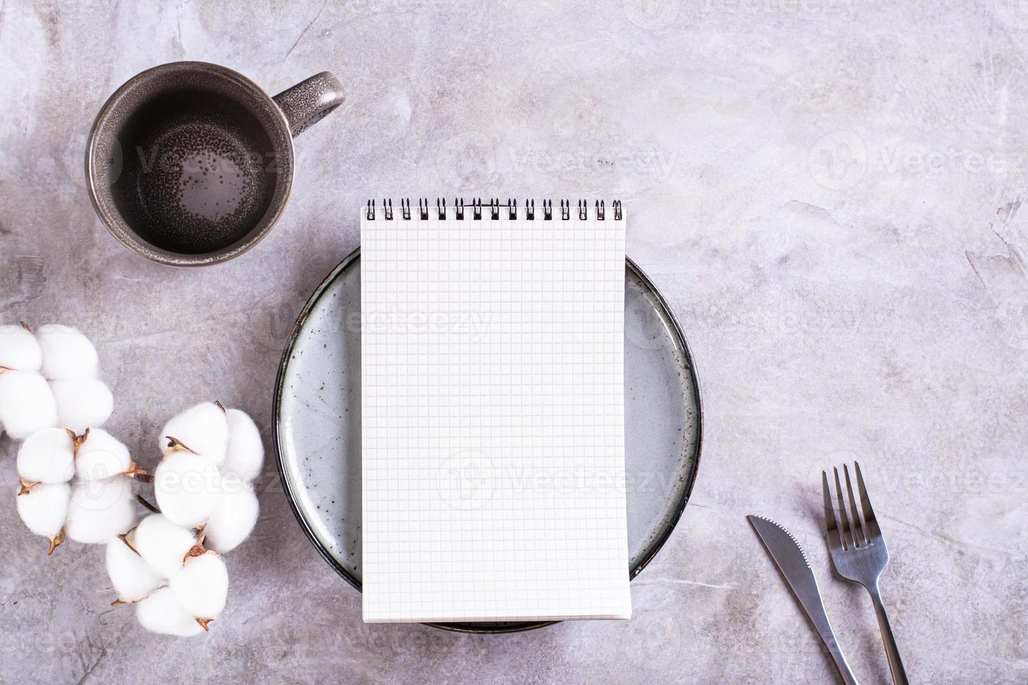 Bosquejo de un cuaderno en un lámina, un vacío taza y un rama de algodón en un gris antecedentes parte superior ver foto