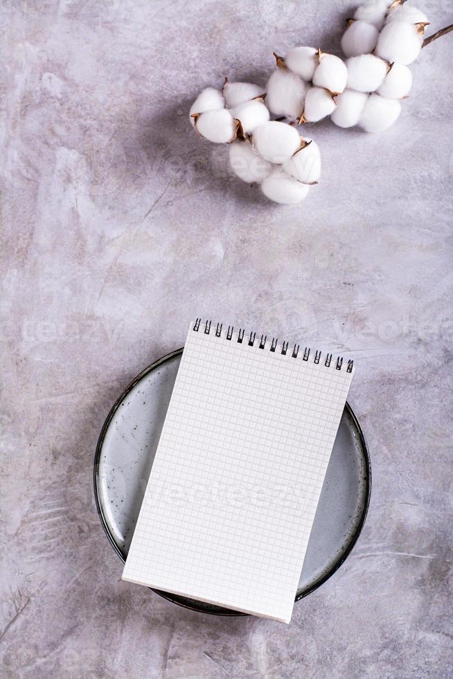 Mockup of an open notebook on a plate and a branch of cotton on a gray background top and vertical view photo