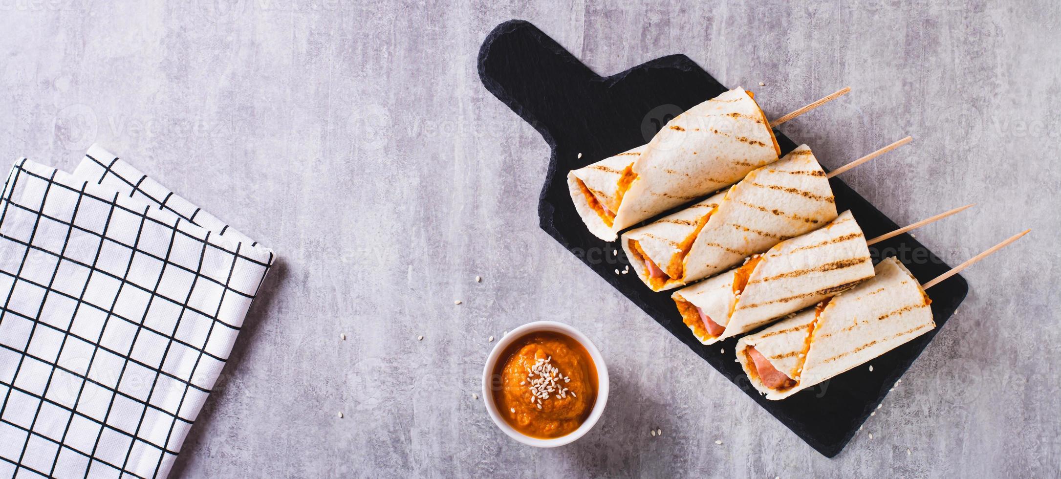 Homemade corn dogs in grilled tortilla with sauce on slate on the table top view web banner photo