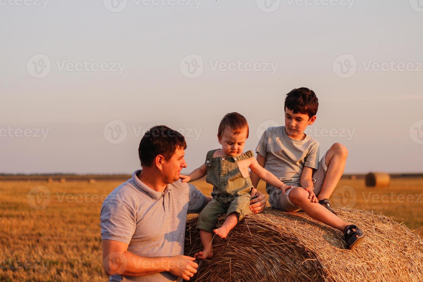 papá con dos hijos en el campo a puesta de sol. concepto de simpático familia y de verano vacaciones foto