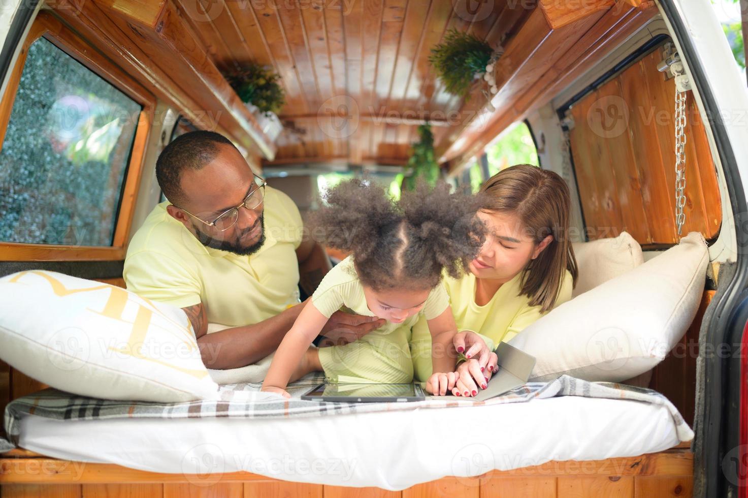 The back of a white classic van, little kids play and learn about the world on their tablet with parents taking care of helping. photo