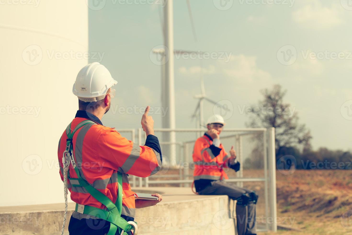 Engineer working at a wind farm for renewable energy has the responsibility of maintaining a sizable wind turbine. Encourage one another as you complete duties. photo