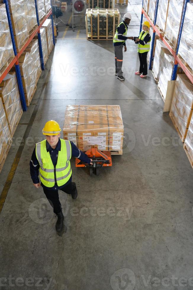 trabajador en auto partes almacén utilizar un carretón a trabajo a traer el caja de auto partes dentro el almacenamiento estante de el almacén esperando para entrega a el coche montaje línea foto