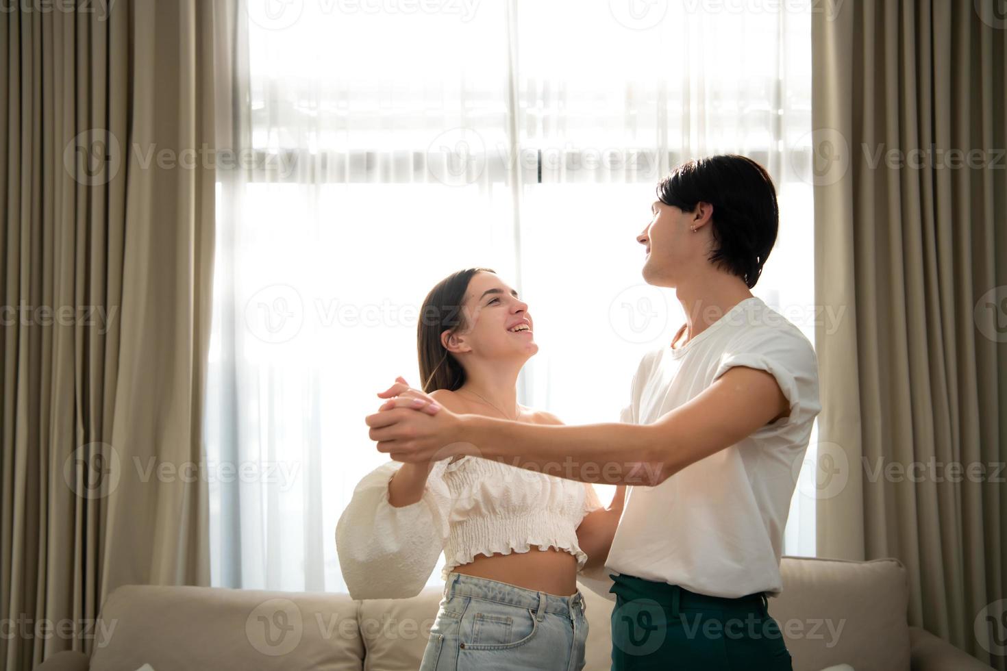 joven Pareja en el vivo habitación de el casa en el mañana, bailando felizmente juntos foto