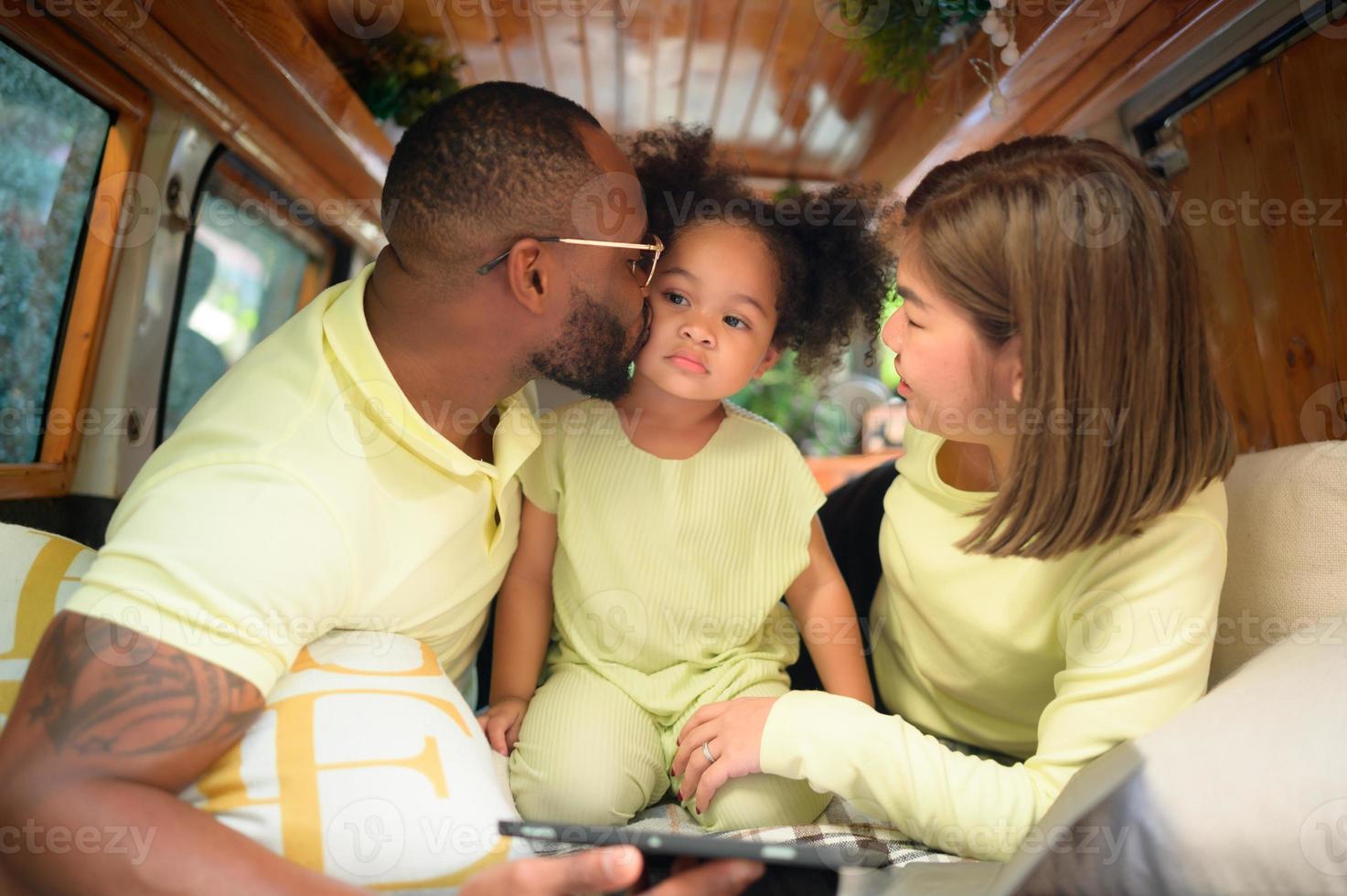 The back of a white classic van, little kids play and learn about the world on their tablet with parents taking care of helping. photo