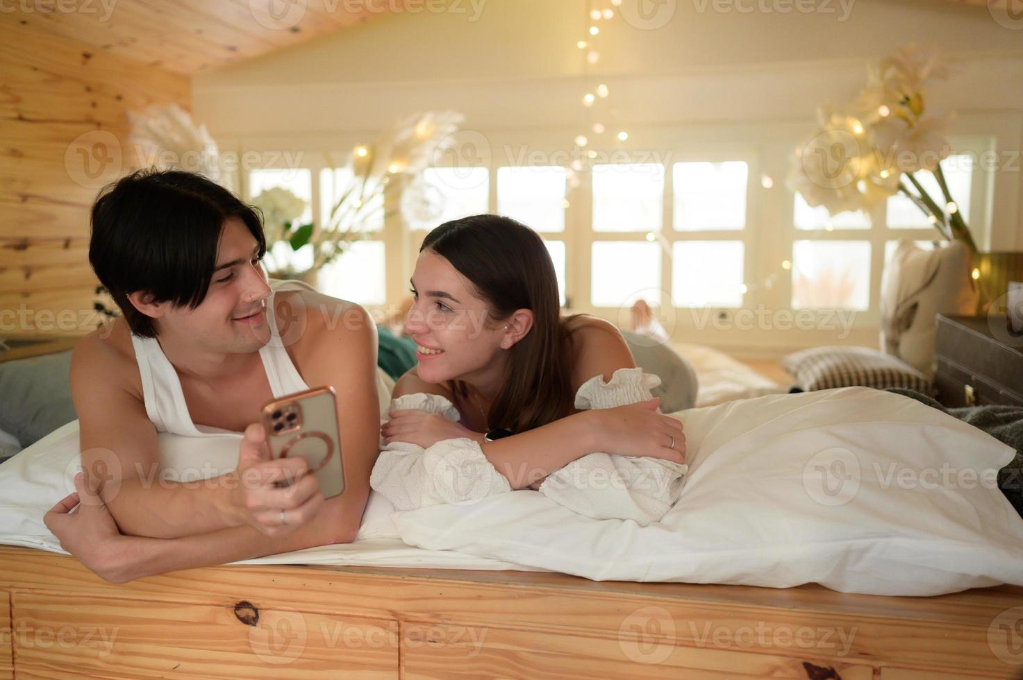 Young couple in the attic bedroom in the morning, Say hi to pals online using smartphone. photo