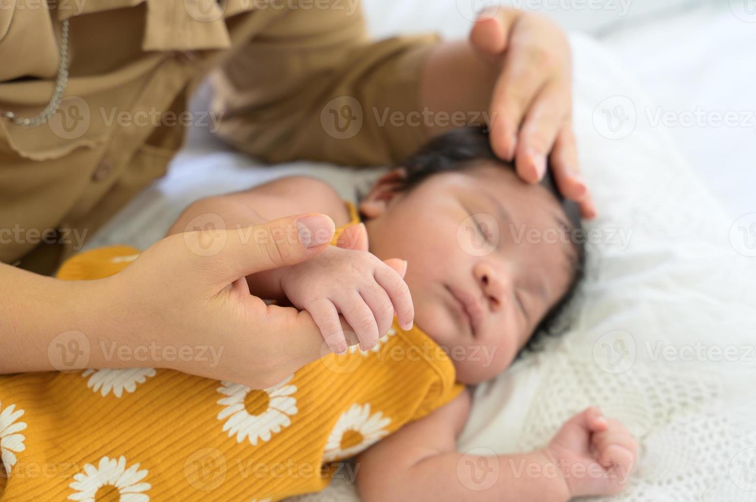 Mother holding hand of newborn baby on white bed.Mom lying down nursing infant girl at home photo